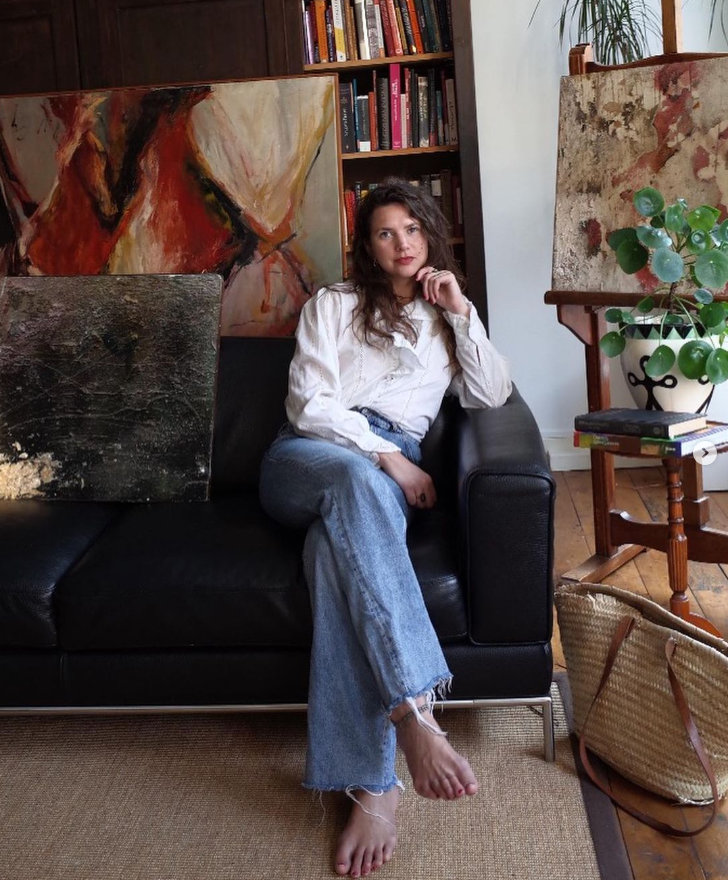 Woman on couch among paintings in cozy art studio.