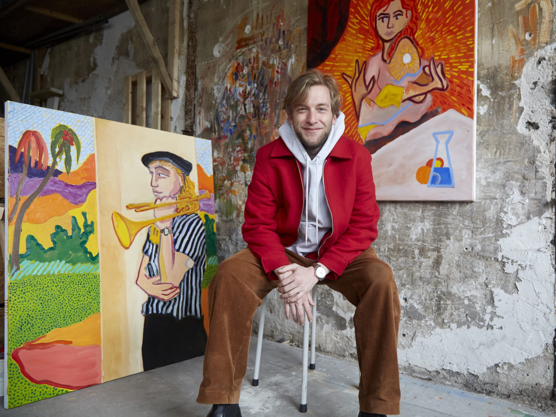 Artist smiles with colorful paintings in studio.