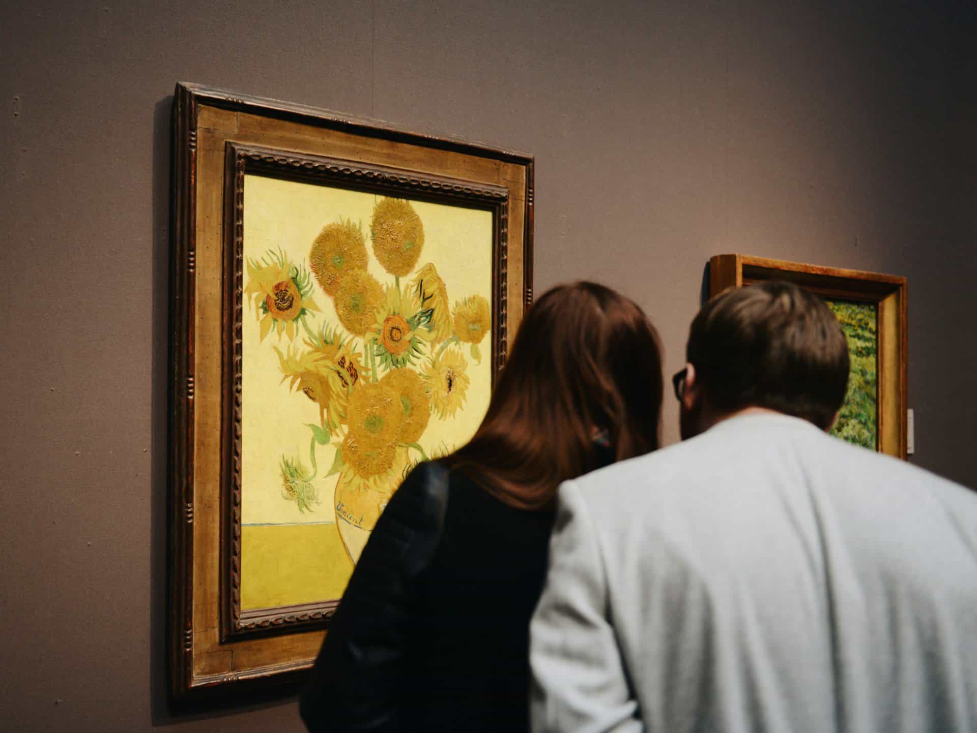 Couple admiring Van Gogh's Sunflowers painting in gallery.